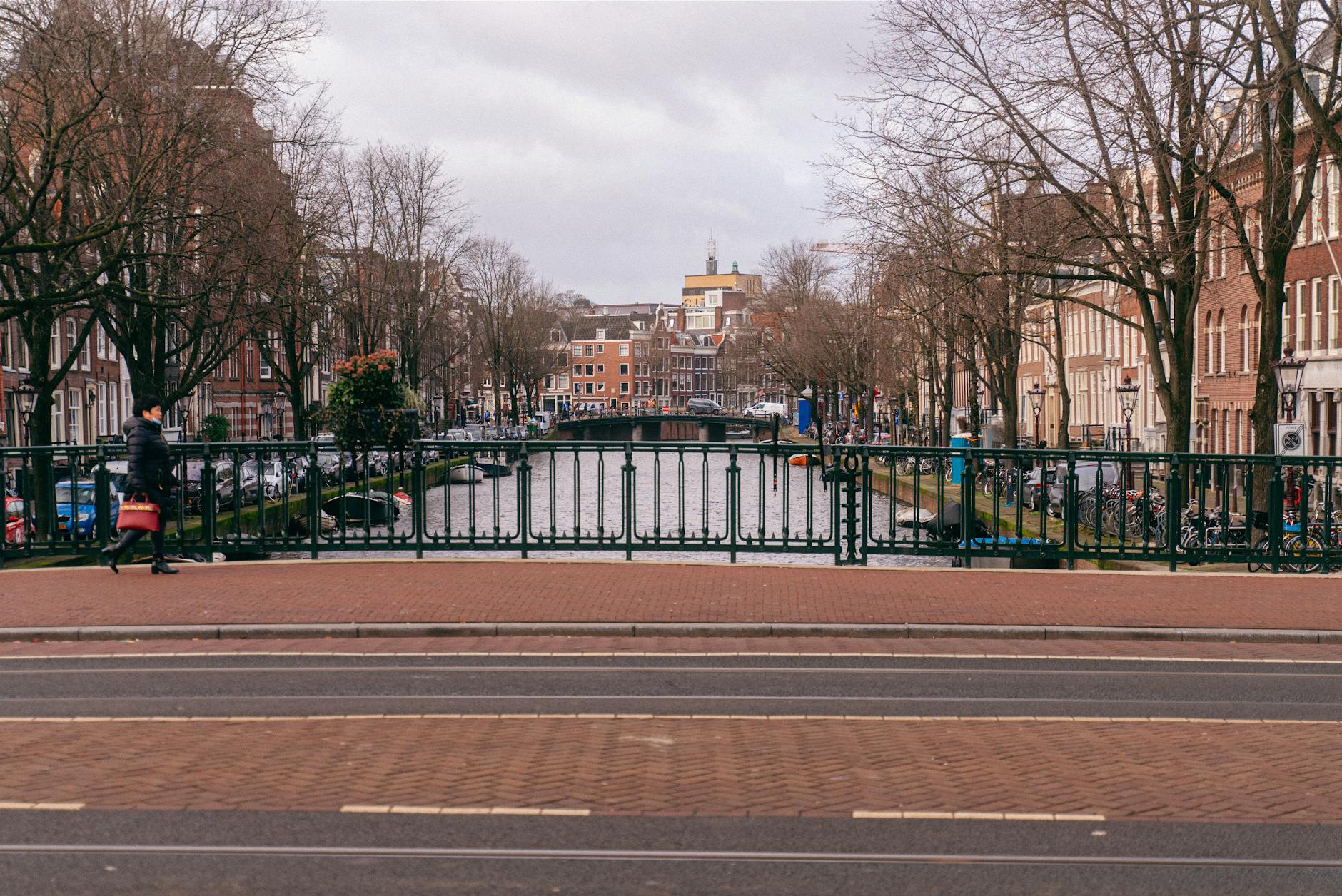 Jak zwiedzać Amsterdam bez tłumów: alternatywne godziny, dzielnice i mniej znane muzea Zimowy kanał w Amsterdamie z pustym mostem i kamienicami w tle