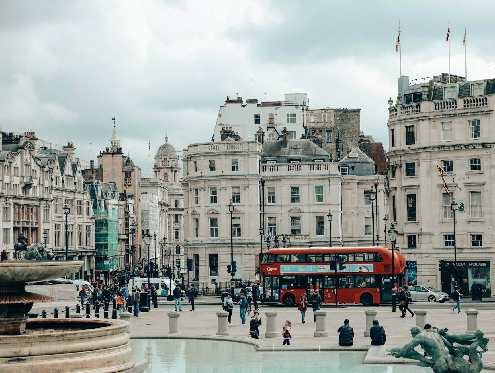 Czerwony piętrowy autobus przy historycznym placu z fontanną w Londynie